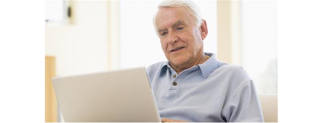 Äldre man sitter med laptop i en soffa.
