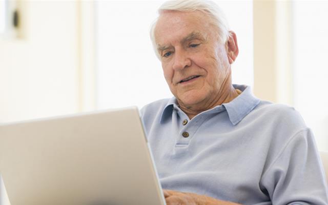 Äldre man sitter med en laptop i knät. 