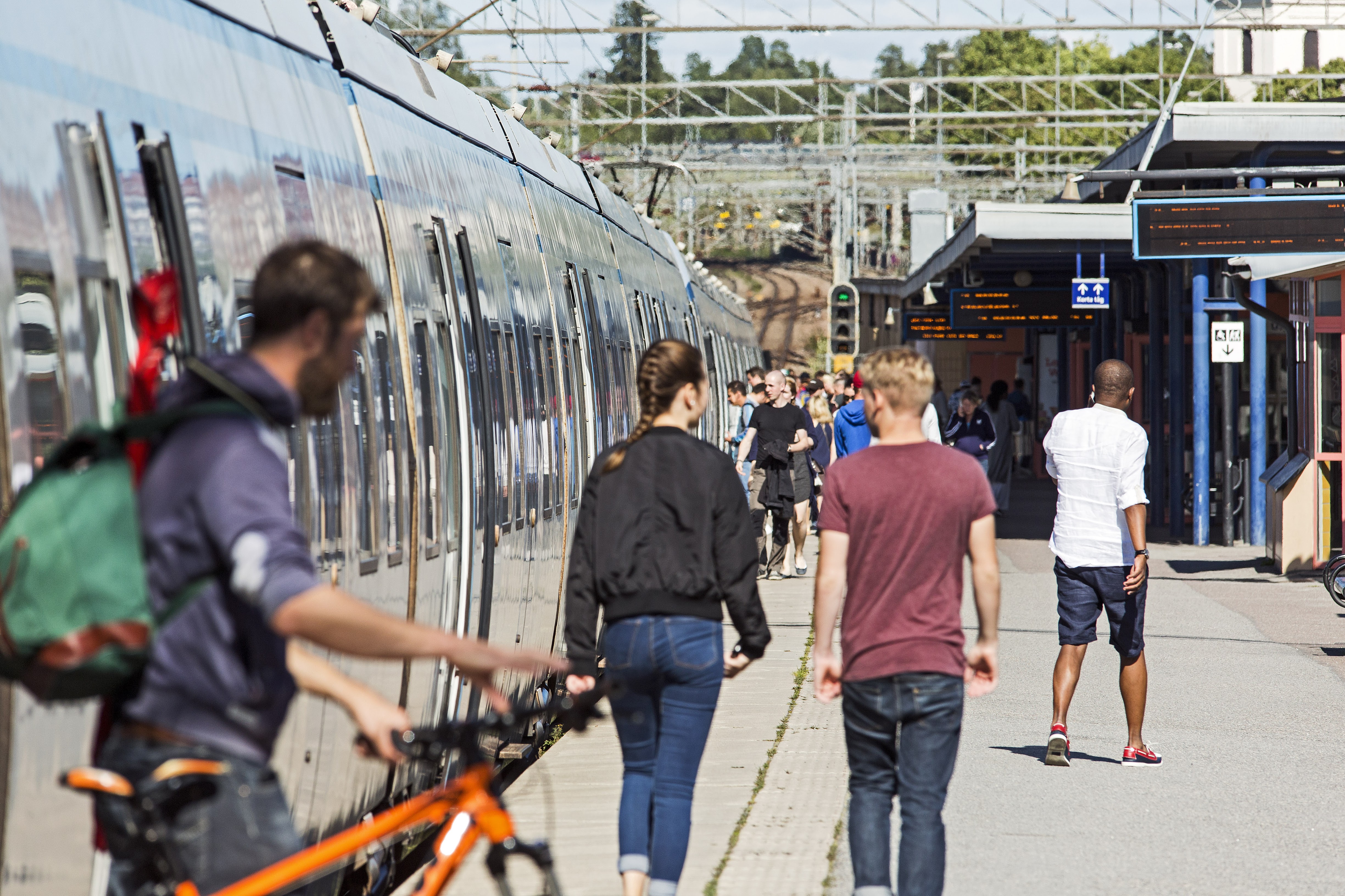 Pendeltåg vid perrong med flera människor som stiger av och på