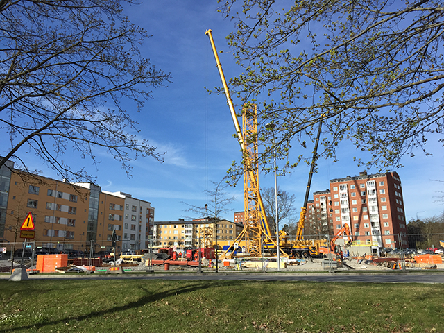 En byggarbetsplats på Kvarnbergsplan i Huddinge. En gul lyftgran och byggställningar syns bland annat.