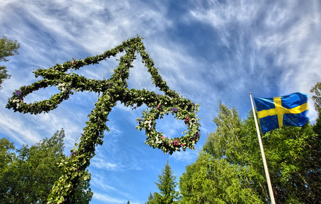 En midsommarstång och svenska flaggan framför blå himmel. Foto: mostphotos.com