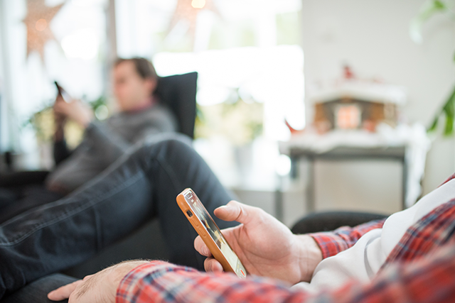 Två män sitter i varsinn fåtölj med mobiltelefon i händerna.