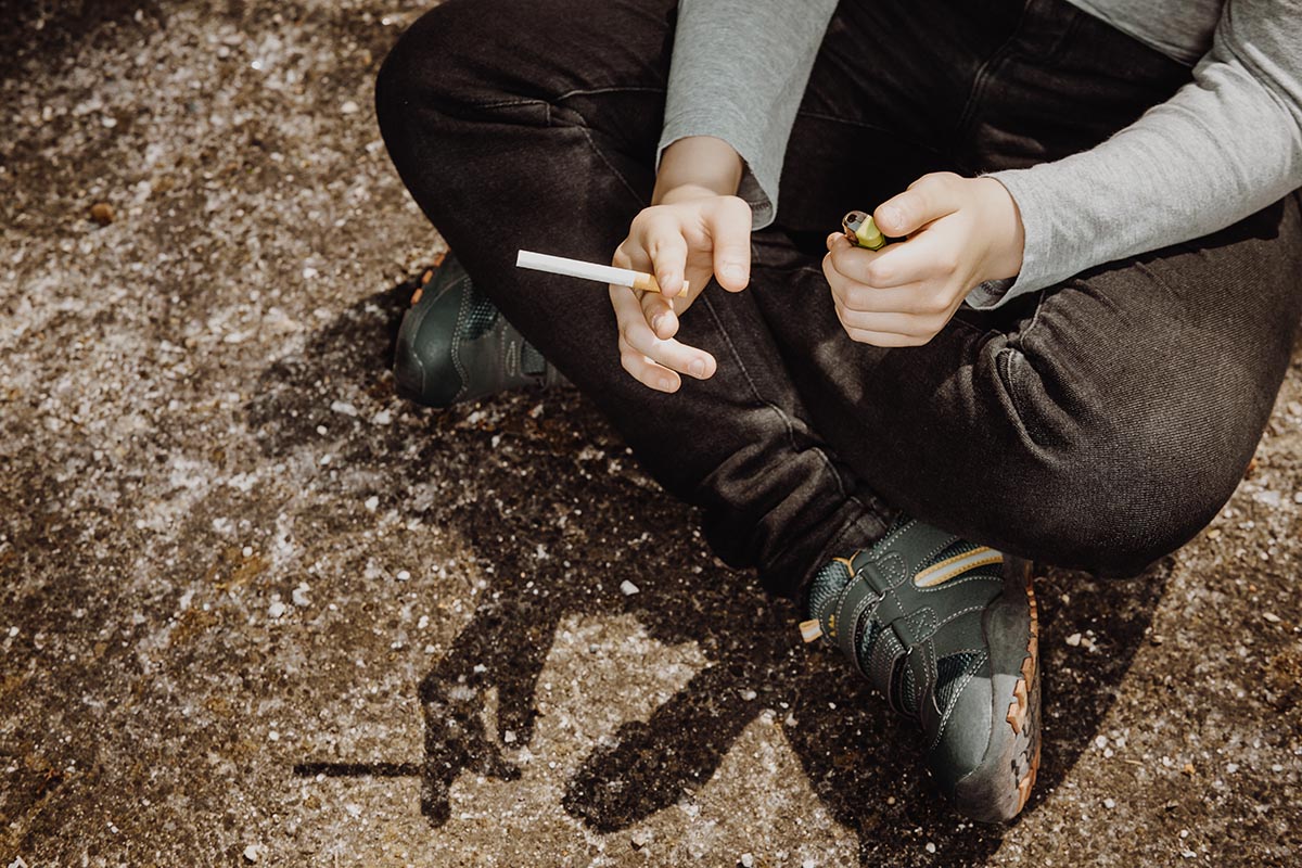 ungdom sitter på marken med cigarett i handen.