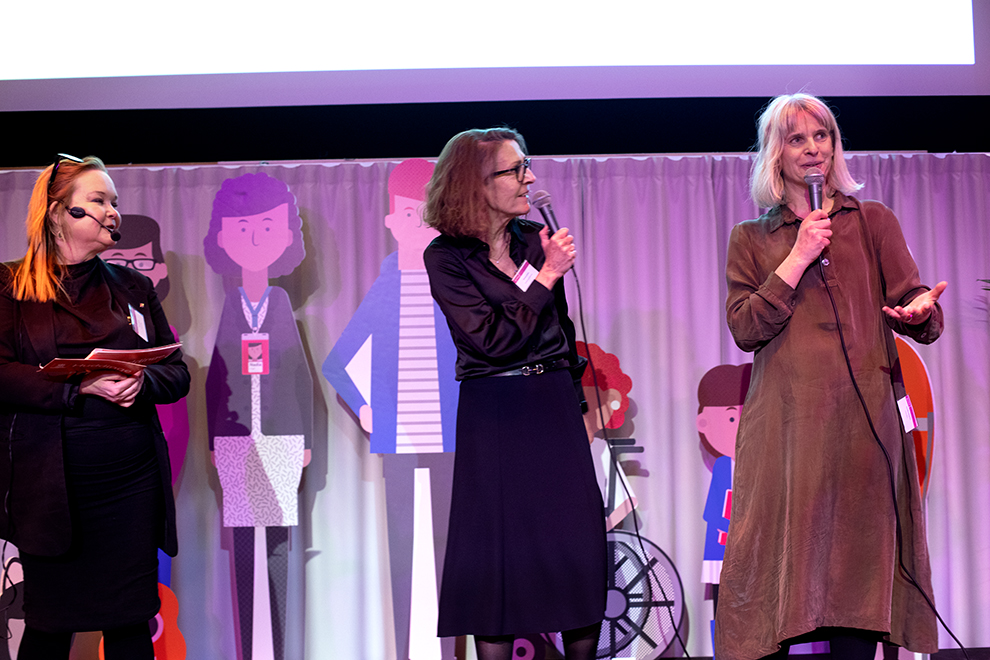 Tre kvinnor står på en scen och pratar i en mikrofon. De är juryn till Huddinge kommuns Kvalitetsgala.